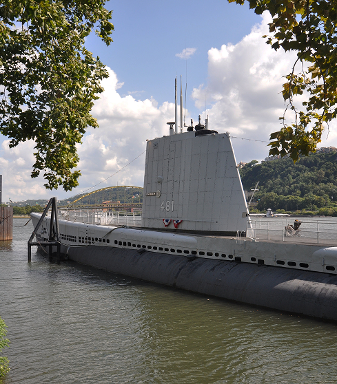 The USS Requin (SS 481) submarine on the river with a bridge in the background.