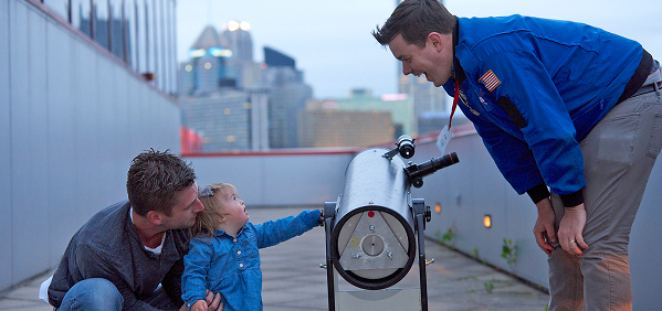 A father and child looking at a telescope with a Science Center staff member on the Science Center rooftop.
