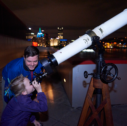 A young girl looks through a telescope on the roof of the Kamin Science Center.