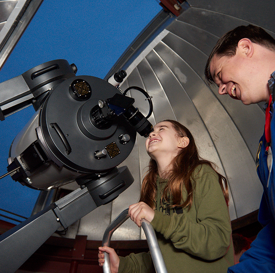 A young girl looks through a telescope in the observatory.
