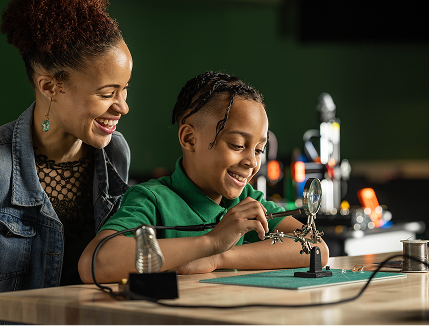 Mother watches son soldering in the BNY Fab Lab.