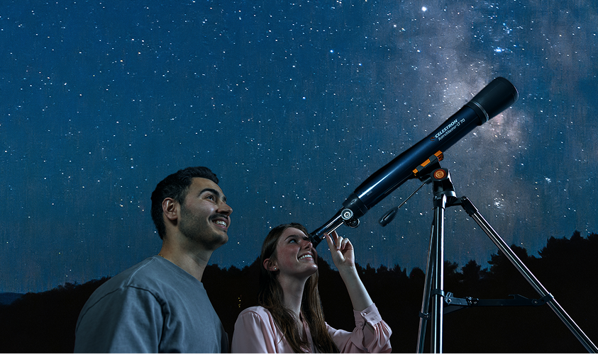 A couple with a telescope looking up at the night sky.