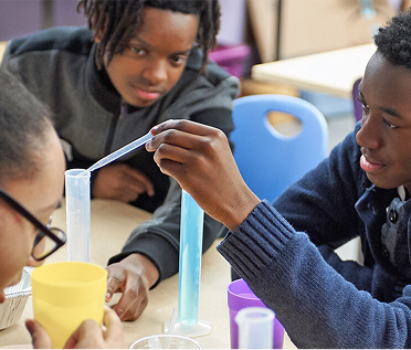 Three young boys are using an eye dropper to add a liquid to a test tube.
