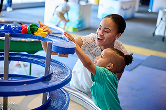 A mother and child playing with boats on a water table
